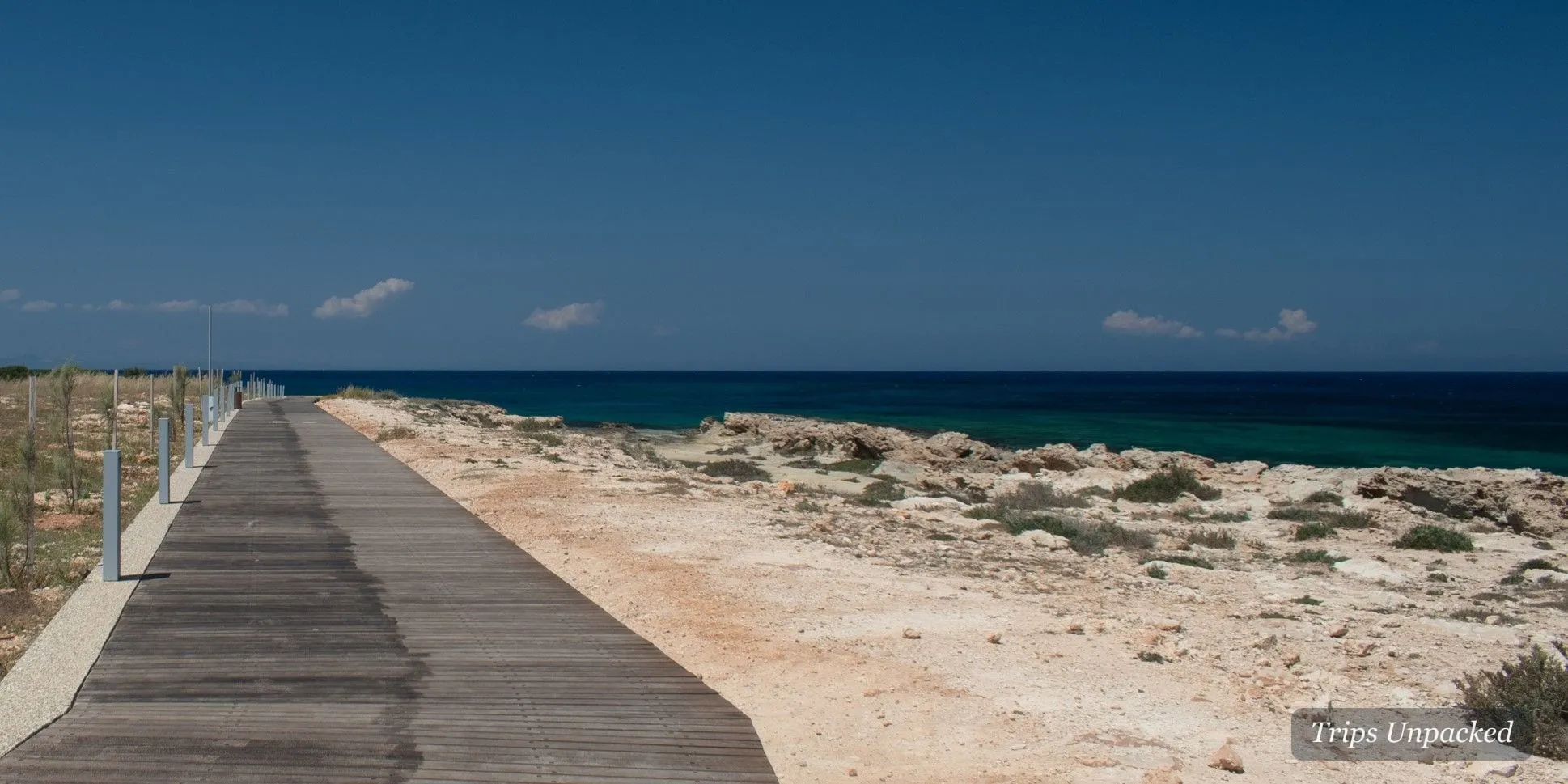 Coastal boardwalk path beside the rocky Cyprus shoreline and deep-blue sea
