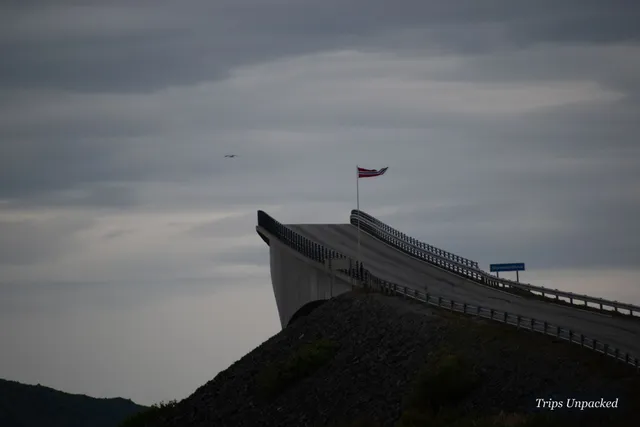 The Atlantic Ocean Road bridge curving into a grey sky, a Norwegian flag flying