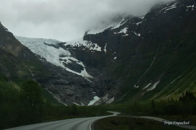 A road curving toward a glacier under a moody mountain sky
