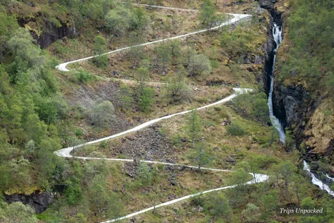 A switchback trail winding down a green mountainside beside a waterfall
