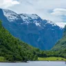 The Nærøyfjord: snow-streaked peaks above steep green slopes falling to still fjord water.