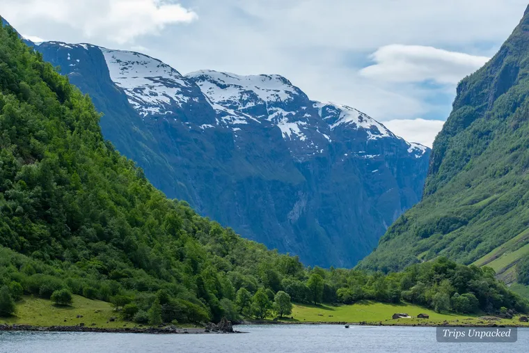 The Nærøyfjord: snow-streaked peaks above steep green slopes falling to still fjord water.
