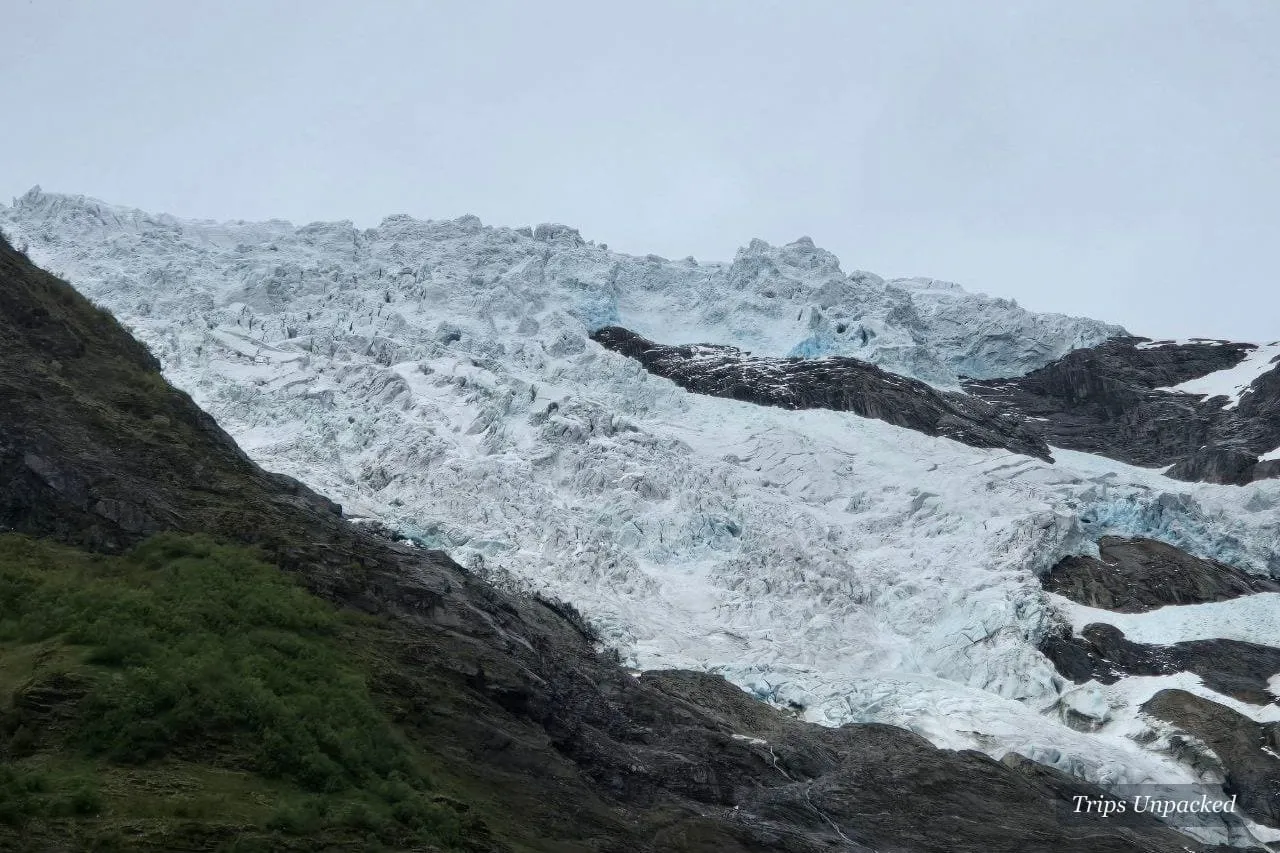 A glacier tongue in blue-white ice between dark rock, seen from the valley floor.