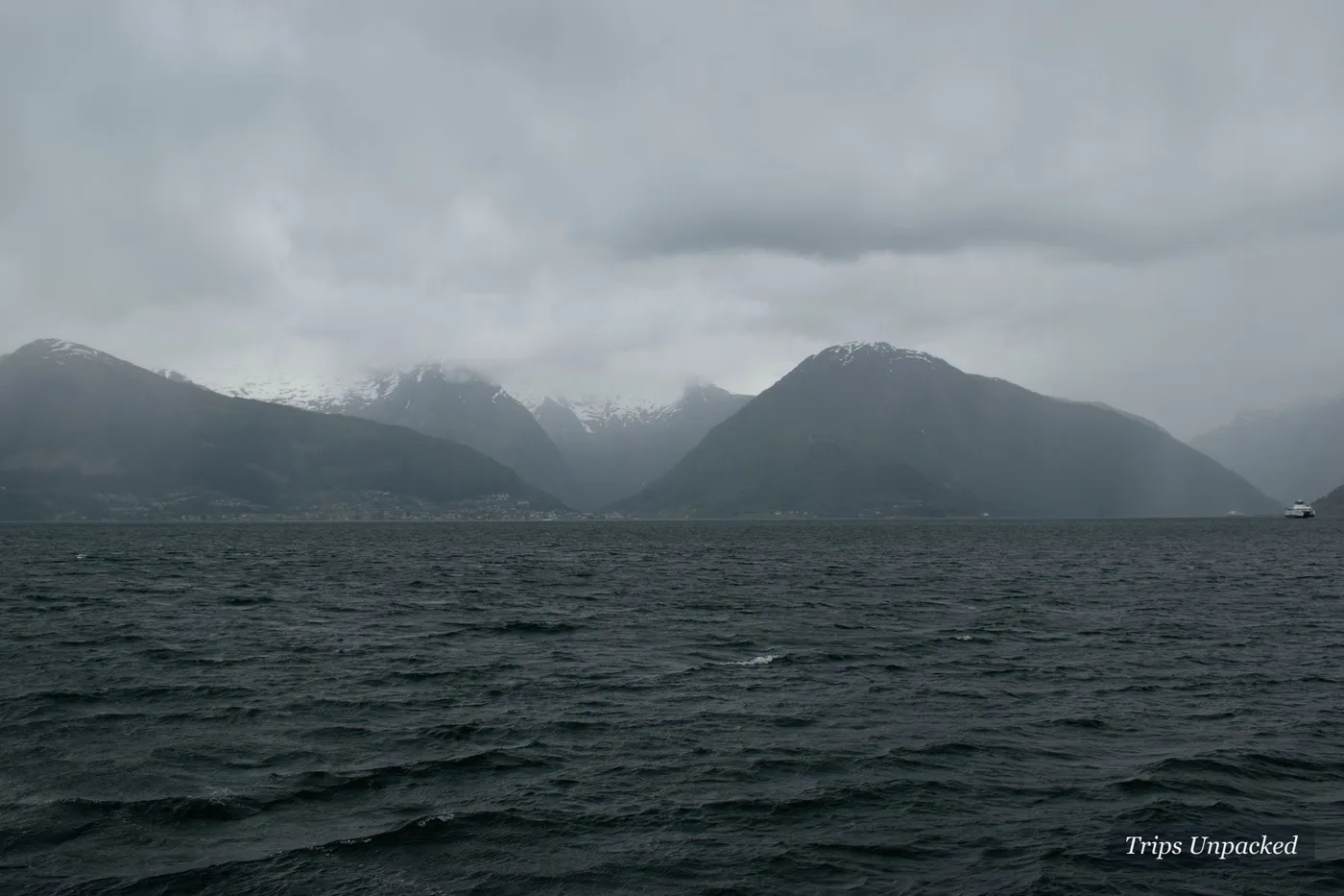 A moody, cloud-wrapped fjord with snow still clinging to the far mountains.