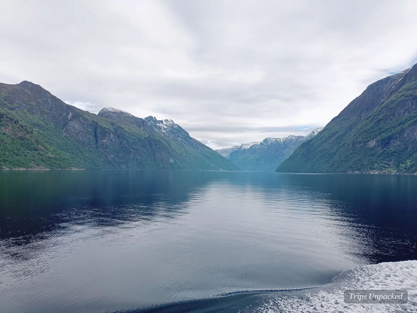 The still, mirror-calm Geirangerfjord stretching between steep green mountainsides.