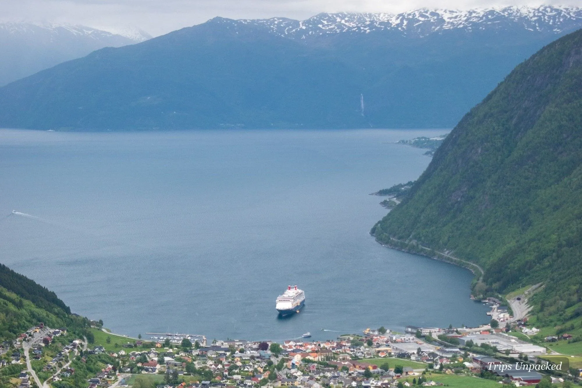 A fjordside town seen from above, a cruise ship anchored on the deep-blue water.