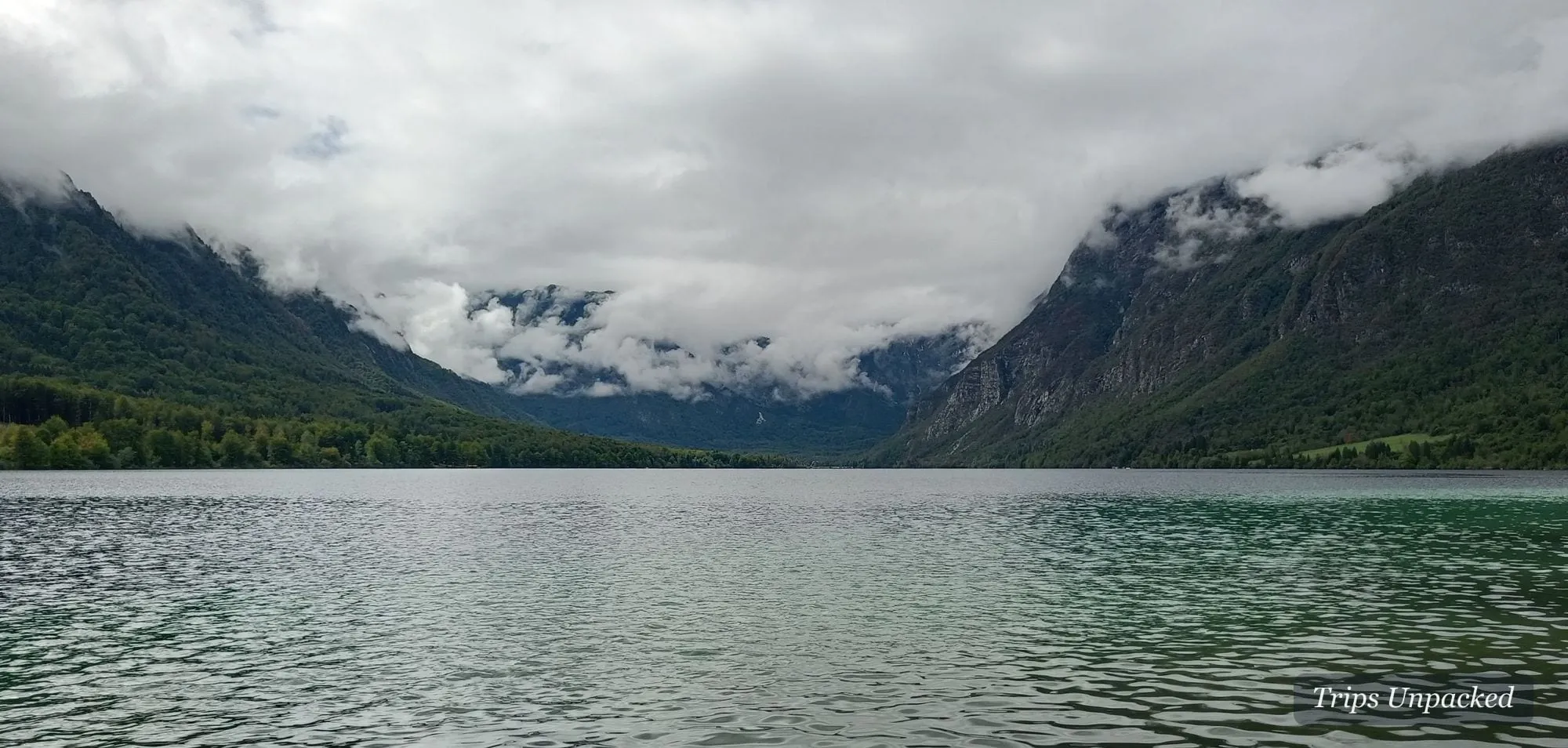 A still Slovenian lake under mountains wrapped in low cloud.