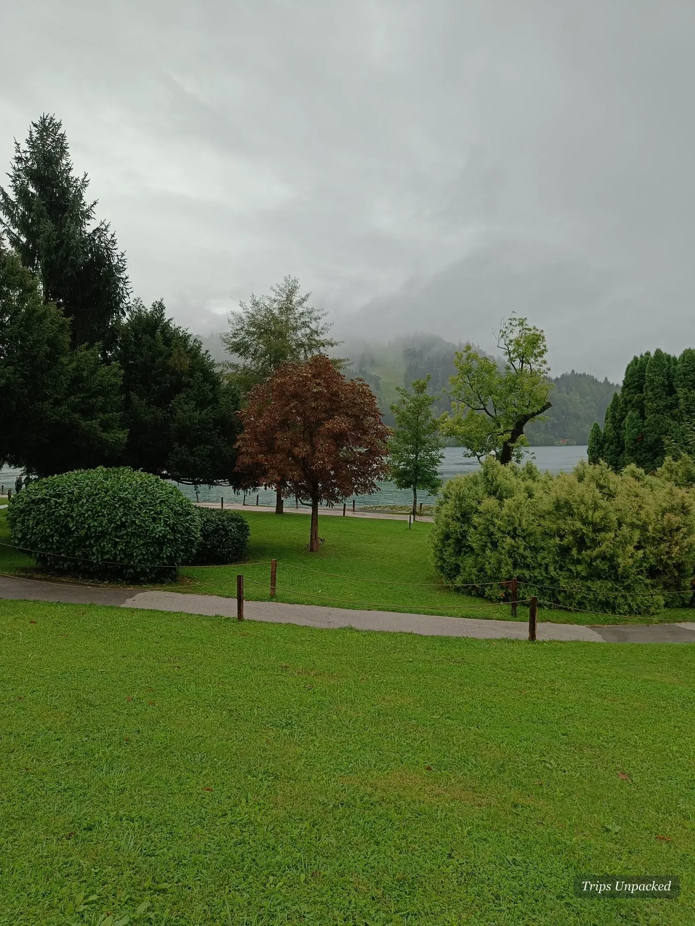 Lawns and trees beside the lake, mist sitting on the hills behind.